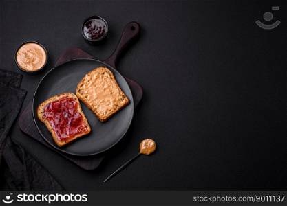 Nutritious sandwiches consisting of bread, raspberry jam and peanut butter on a black ceramic plate on a dark concrete background