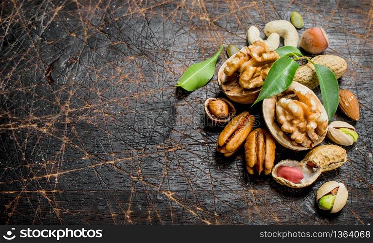 Nuts background. Assortment of different nuts with green leaves . On a wooden background.. Nuts background. Assortment of different nuts with green leaves .