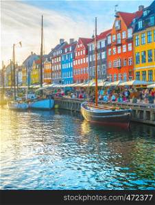 Nyhavn view with boats by embankmentat sunset, people walking and sitting at restaurants, Copenhagen, Denmark