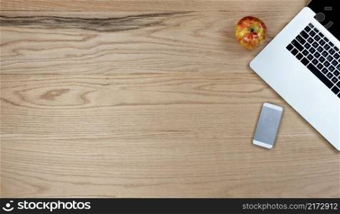 Oak wood office desk table with laptop computer, smartphone and apple fruit for work supplies. Top view with copy space in flat lay format. 