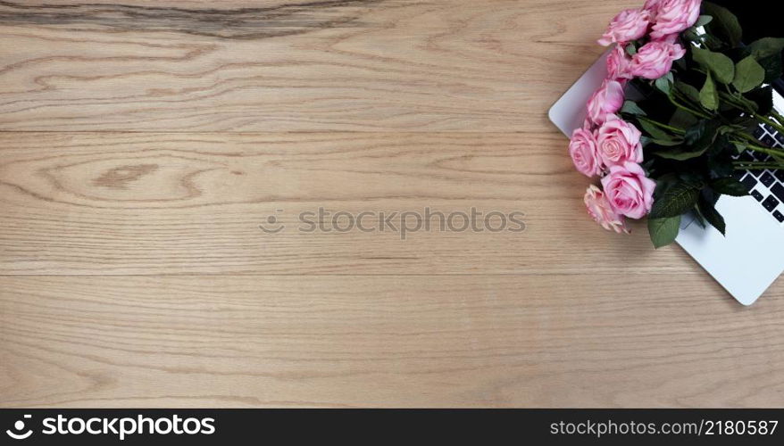 Oak wood office desk table with lovely pink roses on top of a laptop computer for a Mothers day gift at work or school.