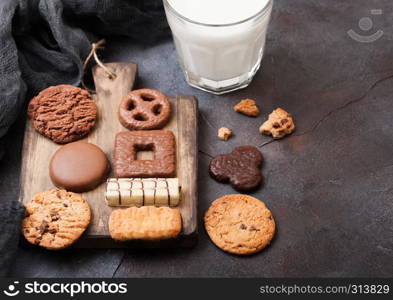 Oat and chocolate cookies selection with glass of milk on wooden board on stone kitchen background
