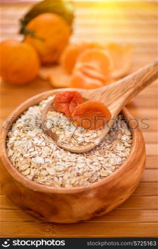 Oat flakes with dried apricots at wooden plate on fruit background