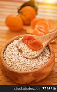 Oat flakes with dried apricots at wooden plate on fruit background