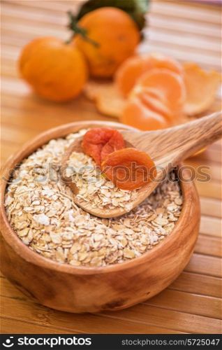 Oat flakes with dried apricots at wooden plate on wooden background