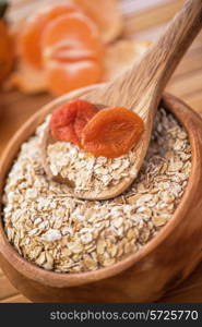 Oat flakes with dried apricots at wooden plate on wooden background