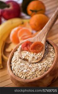 Oat flakes with dried apricots at wooden plate on wooden background. Oat flakes