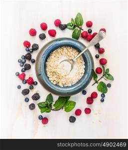 oat flakes with milk and berries in blue rustic bowl with spoon on white wooden background, top view