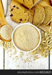 Oat flour in white bowl, oat bran in spoon, oatmeal and stems, bread and biscuits on a background of wooden boards on top