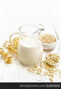 Oat milk in a jug, flour in bowl, oatmeal in spoon, stalks oaten on the background of light board 