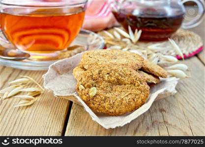 Oatmeal cookies with a stalk of oats on the paper, a cup of tea and teapot, napkin wooden boards background