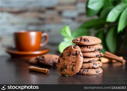 Oatmeal cookies with chocolate on the table against the background of a cup of coffee and green leaves. Breakfast or morning coffee concept. Oatmeal cookies with chocolate on the table against background of cup of coffee and green leaves