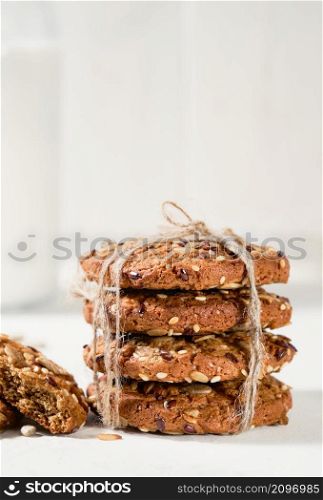 Oatmeal cookies with flax, sunflower and sesame seeds on a white table. Close-up selective focus on cookies. Healthy fitness food concept. Milk and craft biscuits for breakfast