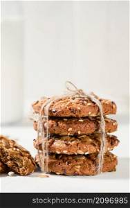 Oatmeal cookies with flax, sunflower and sesame seeds on a white table. Close-up selective focus on cookies. Healthy fitness food concept. Milk and craft biscuits for breakfast
