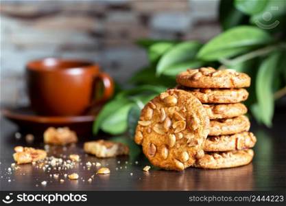 Oatmeal cookies with nuts on a table with a cup of coffee on a background of green leaves. Oatmeal cookies with nuts on table with cup of coffee