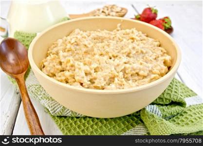 Oatmeal in a bamboo bowl on a green napkin, spoon, strawberries on a light background boards