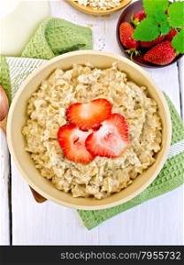 Oatmeal in a bamboo bowl with strawberries on a green napkin, spoon, oat flakes on a background of light board