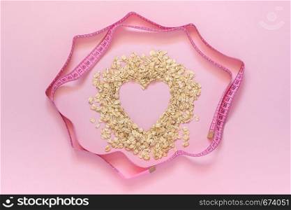 Oatmeal in shape of heart and turn round measuring tape on pink background. Diet concept, Top view Copy space. Oatmeal in shape of heart and turn round measuring tape on pink background. Diet concept