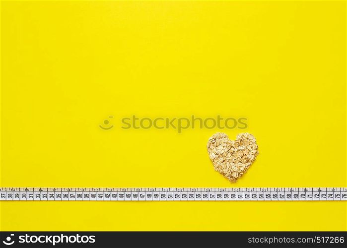 Oatmeal in shape of heart on measuring tape on yellow background. Diet concept, Waist 60 cm. Top view Copy space. Oatmeal in shape of heart on measuring tape on yellow background.
