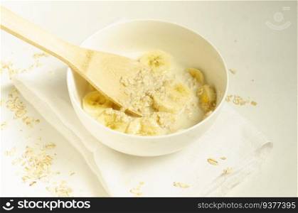 Oatmeal porridge with banana slices with a wooden spoon on white background, minimalistic.Vegetarian healthy breakfast..  Oatmeal porridge with banana slices with a wooden spoon.