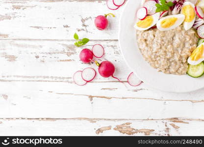 Oatmeal porridge with boiled egg and vegetable salad with fresh radish, cucumber and lettuce. Healthy dietary breakfast