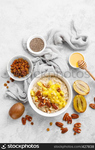 Oatmeal porridge with kiwi fruit, pecan nuts and honey in bowl for breakfast