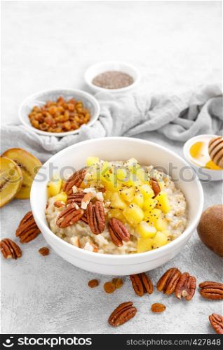 Oatmeal porridge with kiwi fruit, pecan nuts and honey in bowl for breakfast
