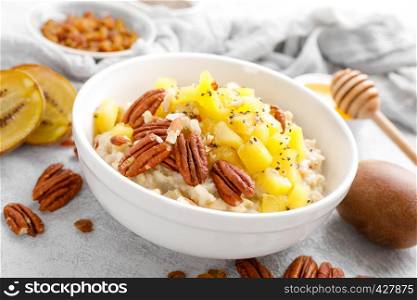 Oatmeal porridge with kiwi fruit, pecan nuts and honey in bowl for breakfast