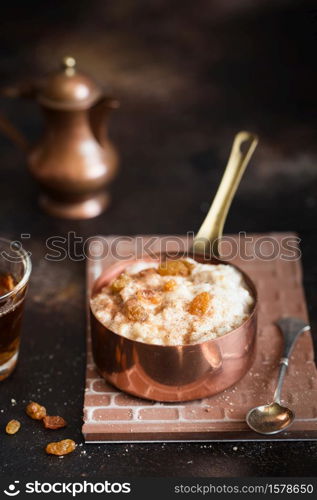 Oatmeal porridge with raisins and cinnamon in a copper cocotte. Oatmeal for breakfast. Vintage style photography