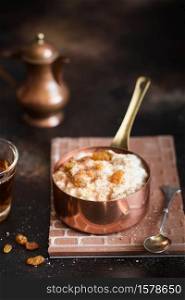 Oatmeal porridge with raisins and cinnamon in a copper cocotte. Oatmeal for breakfast. Vintage style photography