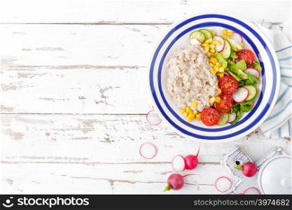 Oatmeal porridge with vegetable salad of fresh tomatoes, corn, cucumber and lettuce. Light, healthy and tasty dietary breakfast. Top view