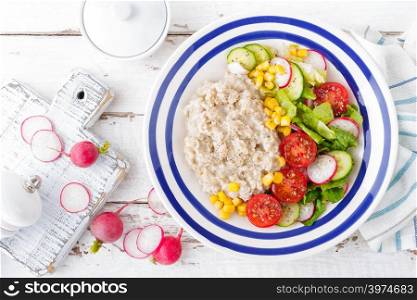 Oatmeal porridge with vegetable salad of fresh tomatoes, corn, cucumber and lettuce. Light, healthy and tasty dietary breakfast. Top view
