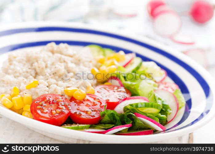 Oatmeal porridge with vegetable salad of fresh tomatoes, corn, cucumber and lettuce. Light, healthy and tasty dietary breakfast. Top view