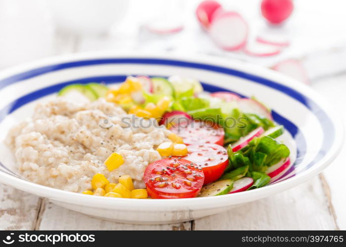 Oatmeal porridge with vegetable salad of fresh tomatoes, corn, cucumber and lettuce. Light, healthy and tasty dietary breakfast. Top view