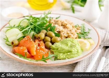 Oatmeal with salted salmon, avocado guacamole and fresh vegetable salad of arugula, cucumbers and olives. Breakfast