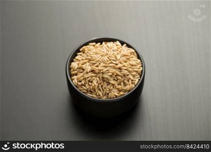 Oats rice in a small black bowl on a black wooden table.