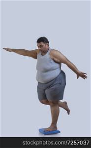 Obese man balancing on weighing scale with one leg with his hands spread across
