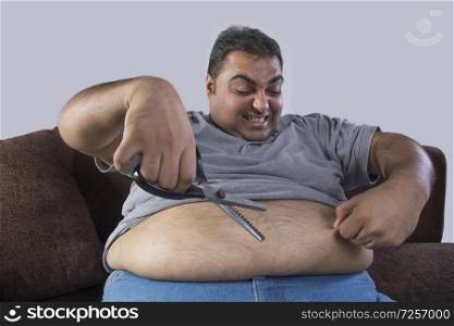 Obese man holding scissors in one hand and belly fat in other with intention to cut excess fat
