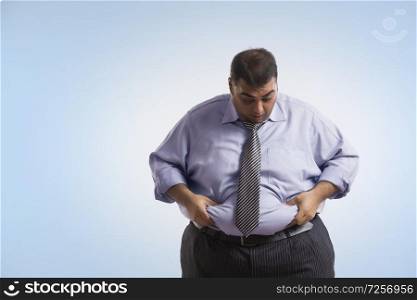 Obese man in formal clothes holding his belly fat with both hands giving an expression of shock
