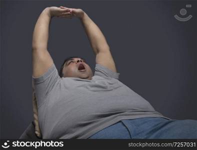 Obese man sitting on chair stretching his arms and yawning