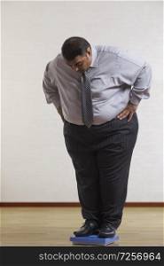 Obese man wearing formal clothes checking his weight on weighing machine standing with hands on waist