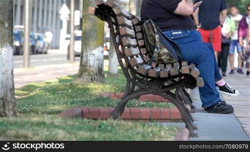 Obese tourist sits on a park bench in Spain