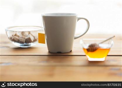 objects and drinks concept - close up tea cup with honey and sugar on wooden table. close up tea cup with honey and sugar on table