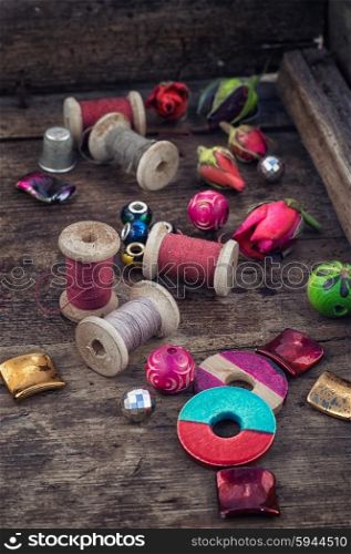 Objects for needlework. Bright beads and thread on wooden stand covered with rosebuds.