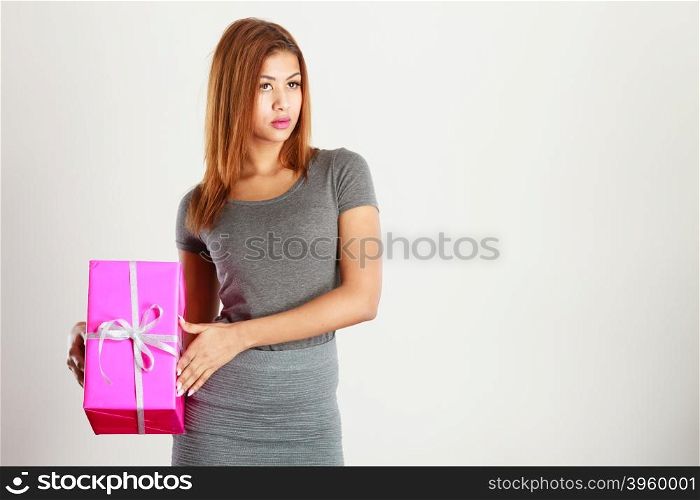 Occasions gifts people concept. Beautiful woman with pink gift. Young blonde lady wearing nice gray outfit, top and skirt. Girl is mixed race.