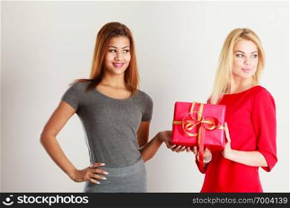 Occasions gifts people concept. Beautiful women blonde caucasian girl and mulatto with red gift box on gray. Two beautiful women with red gift box