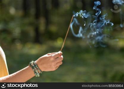 occult science and supernatural concept - close up of hand with smoking incense stick performing magic ritual in forest. hand with smoking incense stick in forest