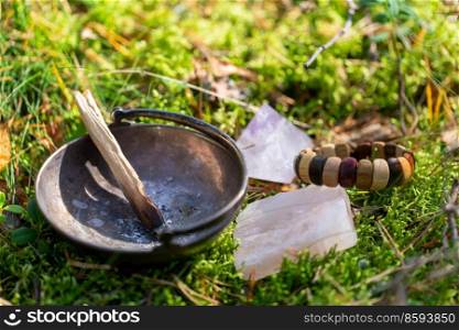 occult science and supernatural concept - close up of palo santo stick in cup and crystal for magic ritual in forest. palo santo stick in cup and crystal in forest