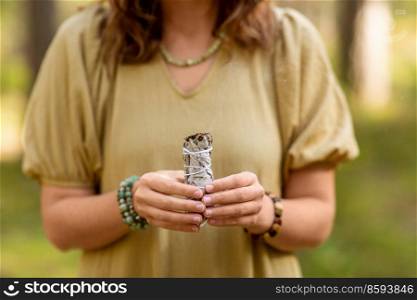 occult science and supernatural concept - close up of woman or witch with smoking white sage performing magic ritual in forest. woman with sage performing magic ritual in forest
