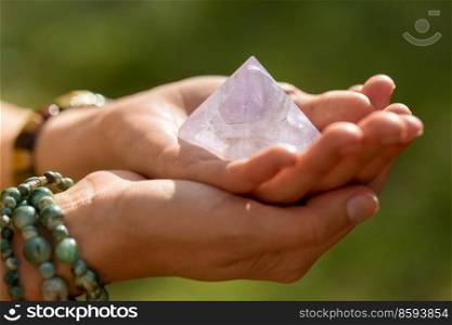 occult science and supernatural concept - close up of woman or witch with semiprecious crystal or gemstone pyramid performing magic ritual in forest. close up of hands holding crystal pyramid